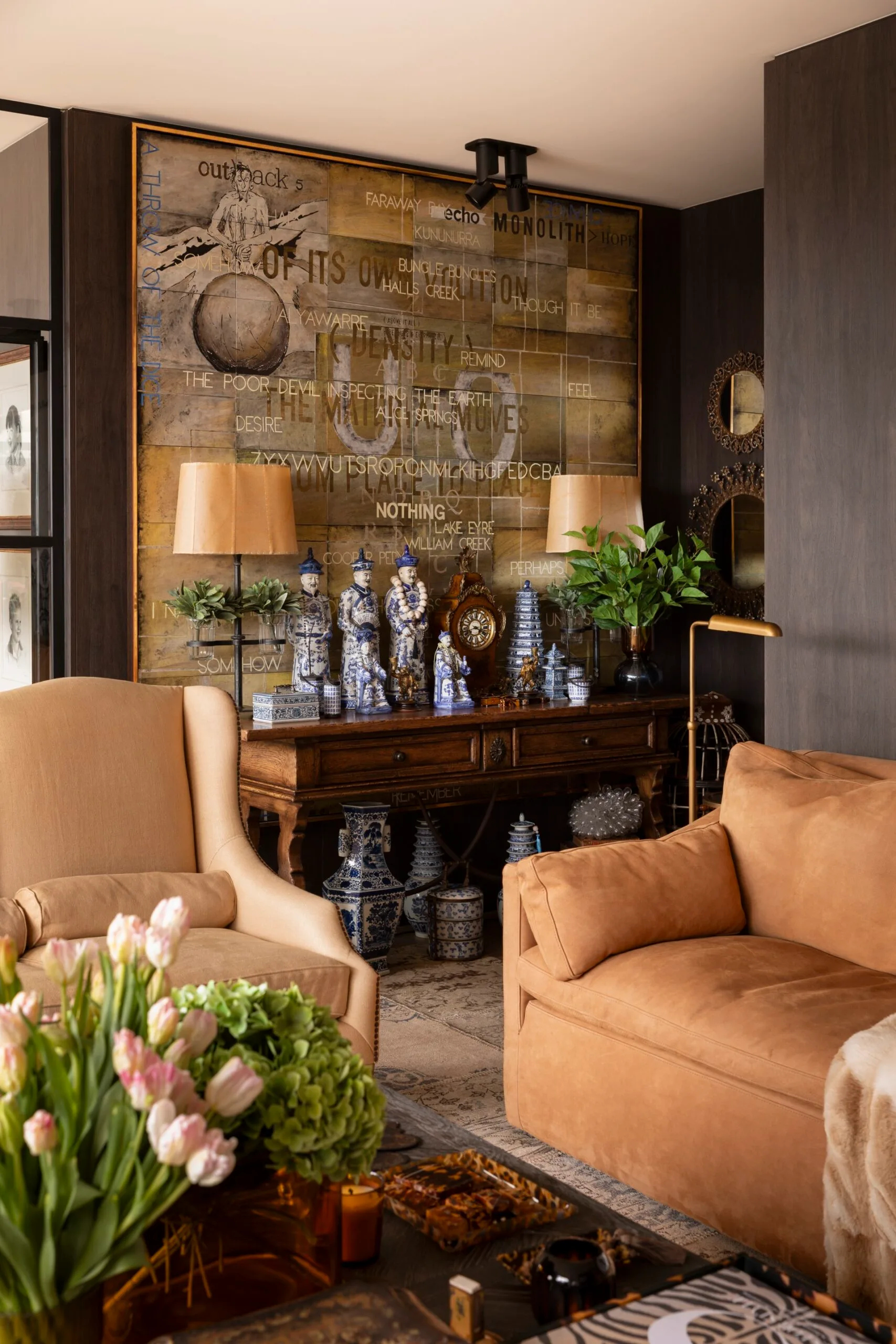 Luxurious living room with cream sofas, a wooden console, decorative vases, a large text art piece, and flowers on a table. This is the living room of TV star Chyka Keebaugh.