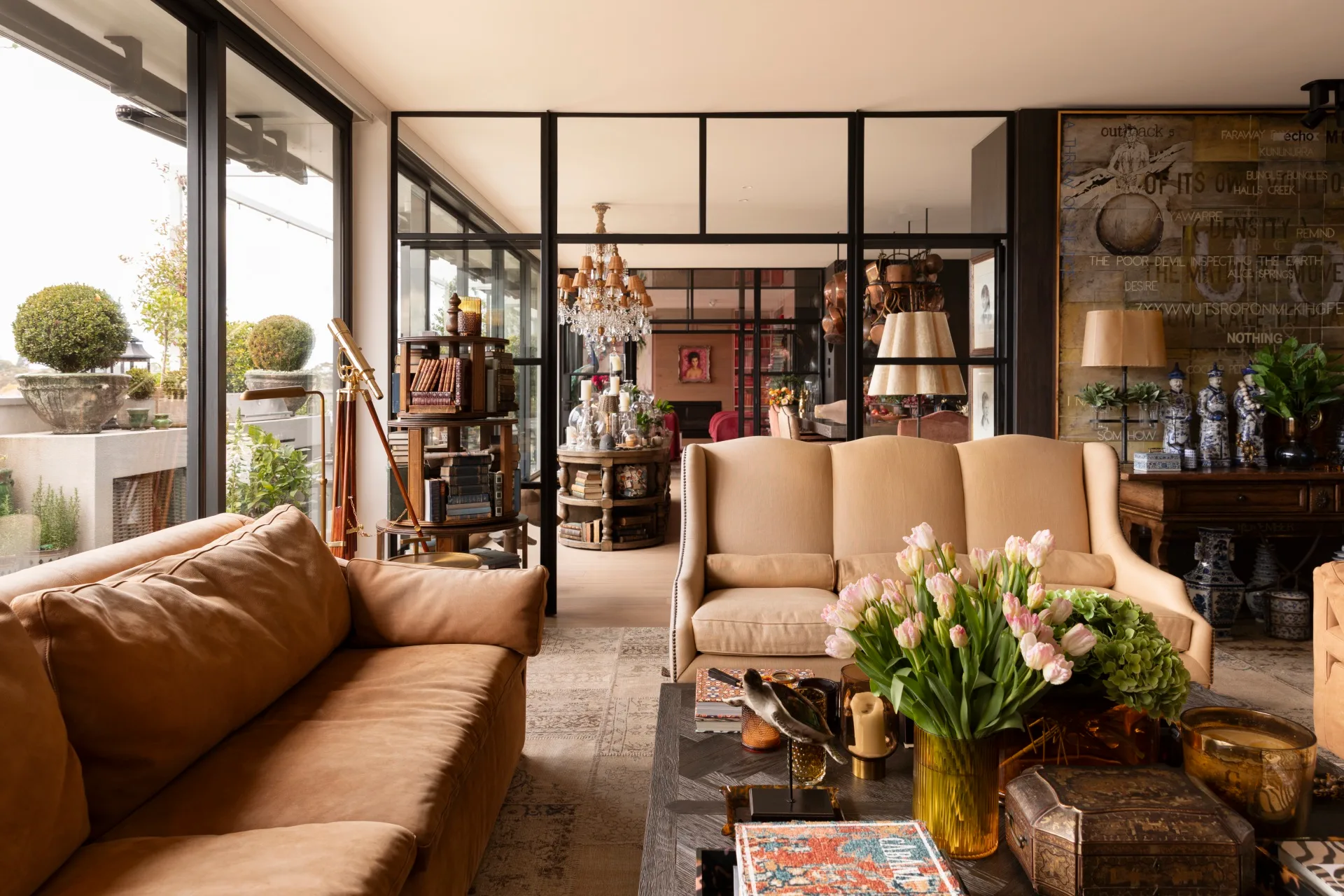 Luxurious living room with leather sofa, tulips on a coffee table, bookshelves, glass doors, and a rooftop view.