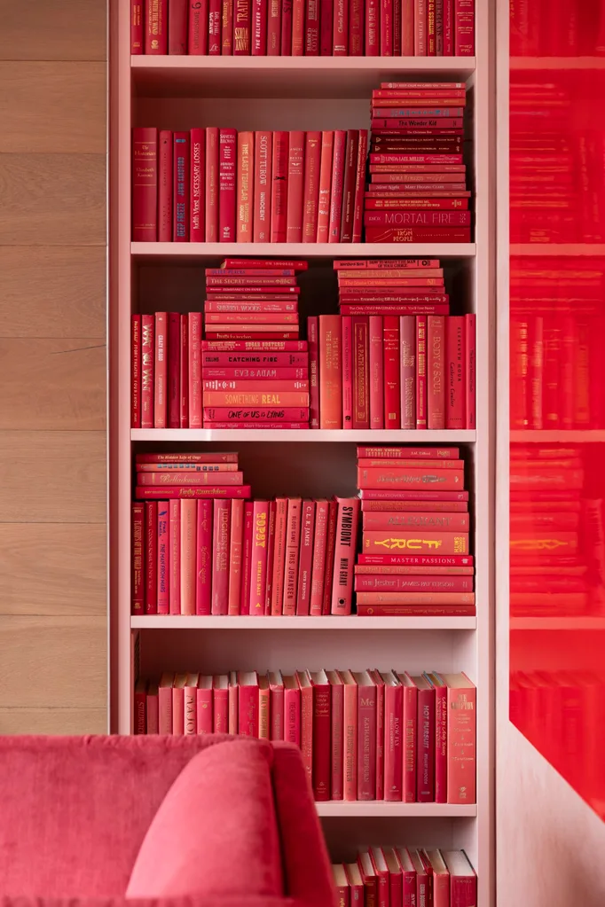 Bookshelf filled with various pink books, with a pink sofa in the foreground.