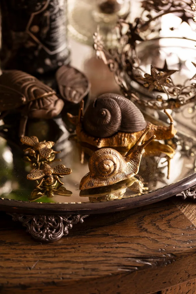 Bronze and gold snail and insect figurines on an ornate mirrored tray with a decorative crown