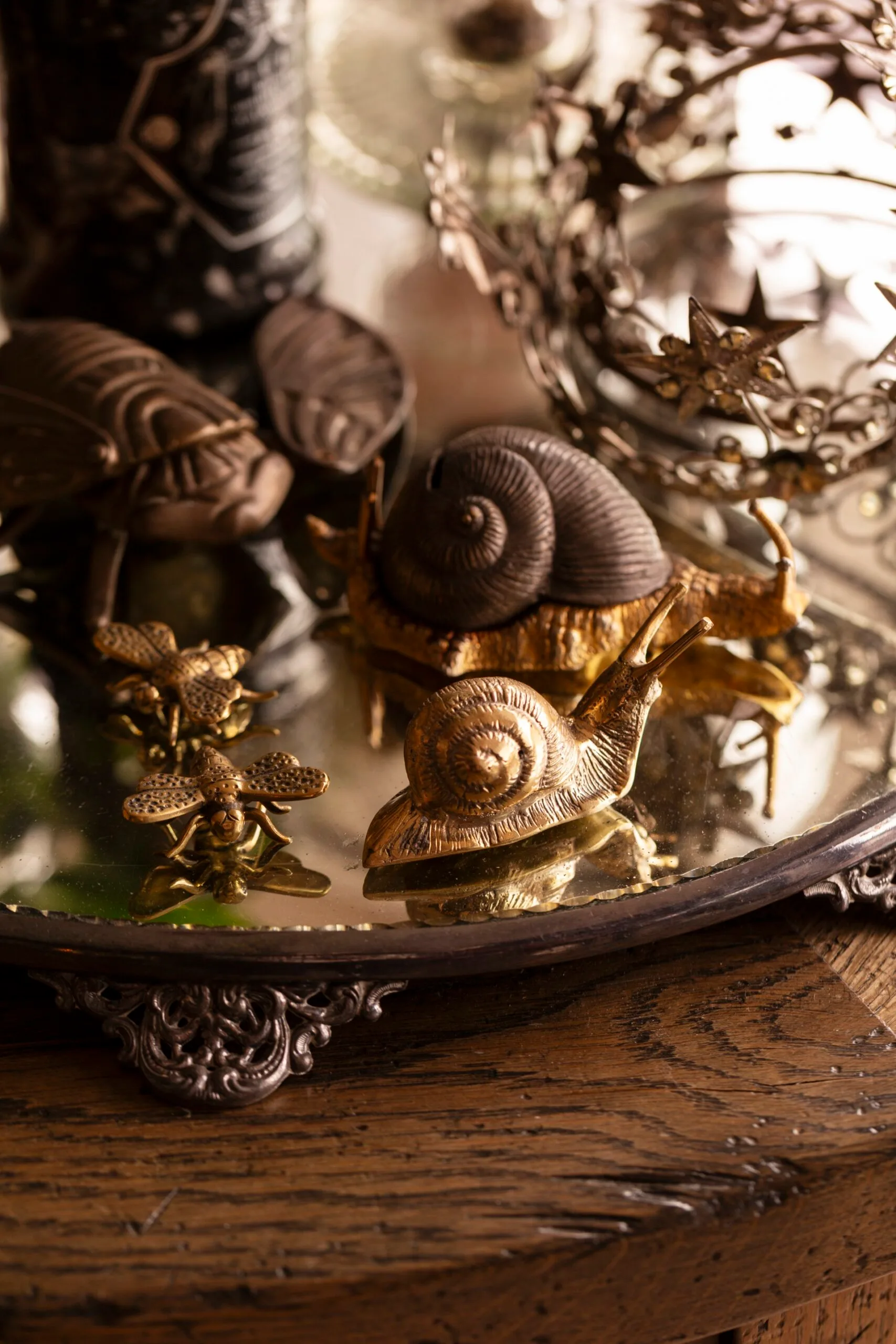 Bronze and gold snail and insect figurines on an ornate mirrored tray with a decorative crown