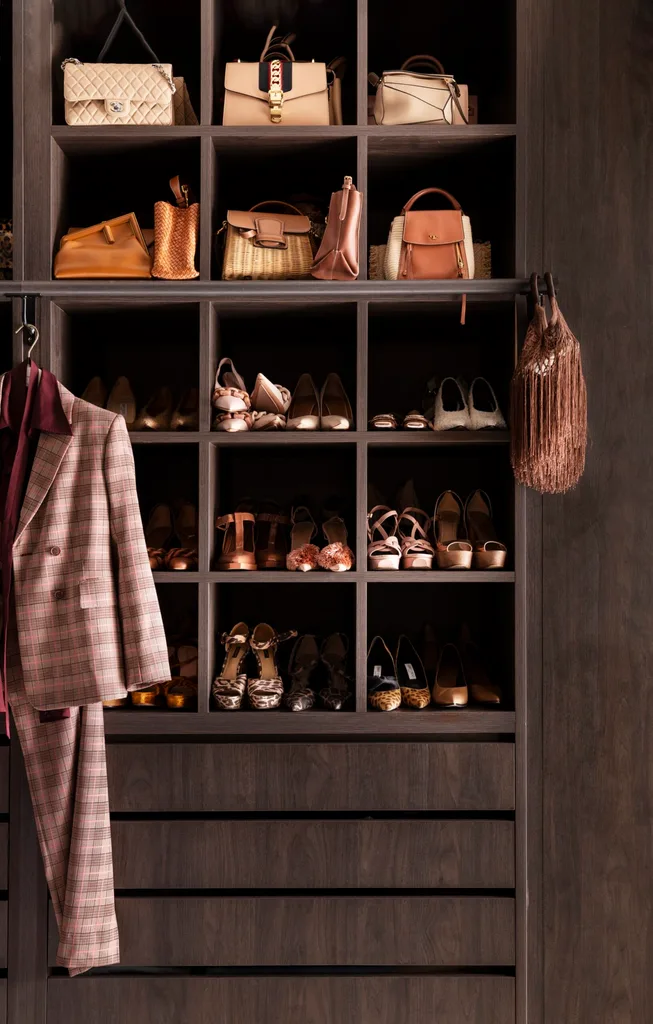 Walk in robe closet with various luxury handbags and shoes, a plaid suit hangs to the side, and a fringe bag hangs on the right.