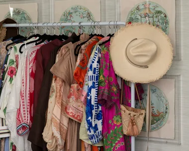 Colorful clothes on a rack with a hat and purse; decorative Asian art on walls; bedroom setting.