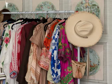 Colorful clothes on a rack with a hat and purse; decorative Asian art on walls; bedroom setting.