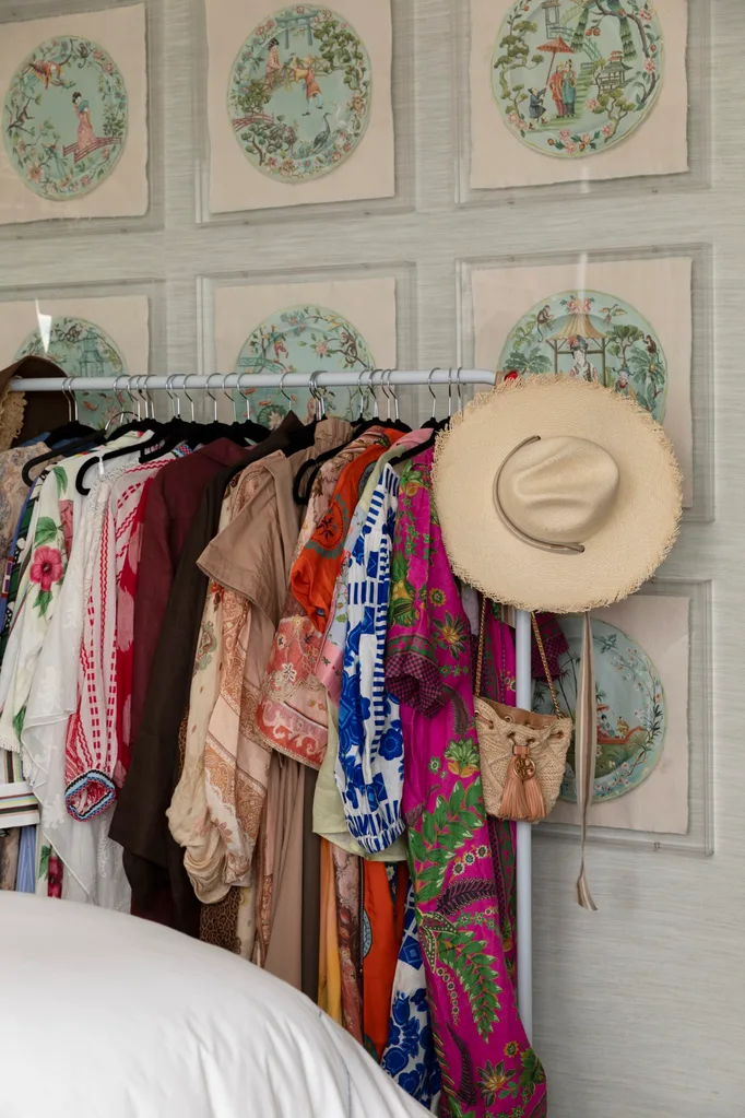 Colorful clothes on a rack with a hat and purse; decorative Asian art on walls; bedroom setting.