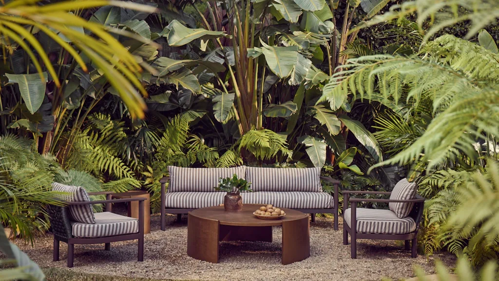 Outdoor seating set with striped cushions in a lush garden surrounded by ferns and tropical plants.