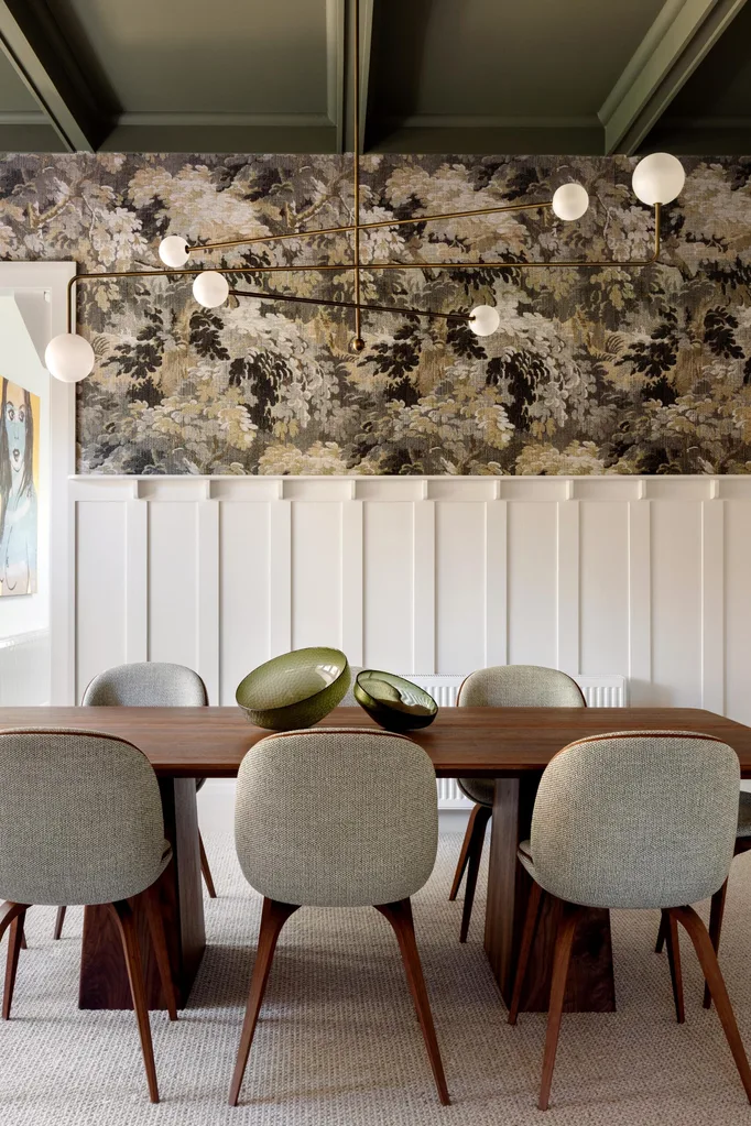 Elegant dining room with a wooden table, six chairs, green glass bowls, floral wallpaper, and modern lighting.