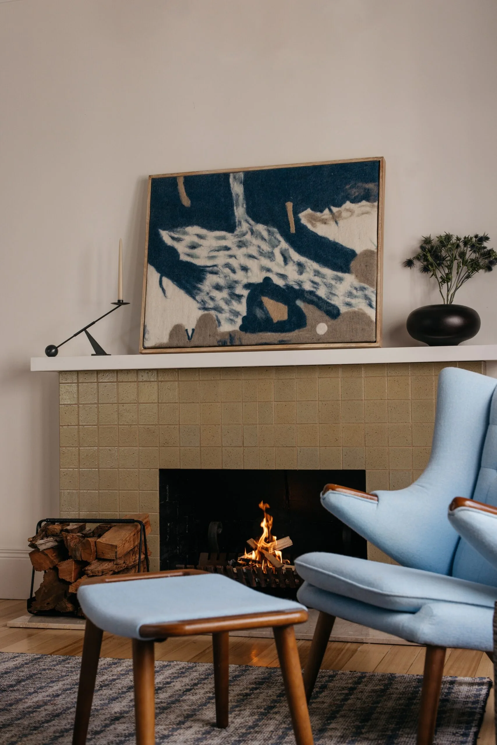 Living room of a heritage home with Scandinavian-style interiors with a neutral palette, vintage furniture, a blue armchair and a wood fireplace.