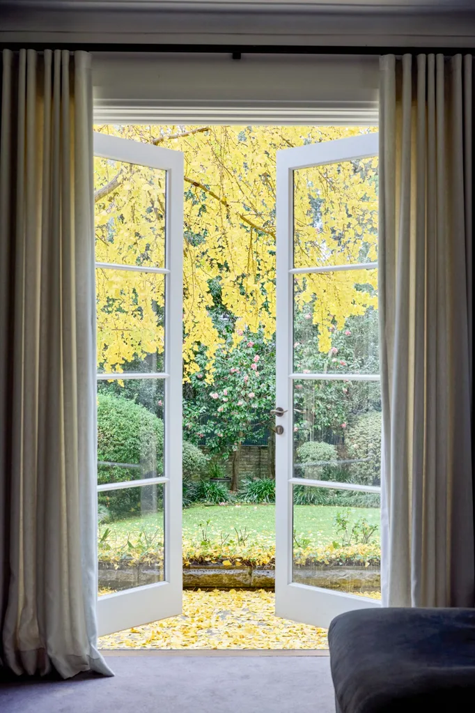 Open white French doors reveal a garden with bright yellow autumn leaves and greenery under a cloudy sky