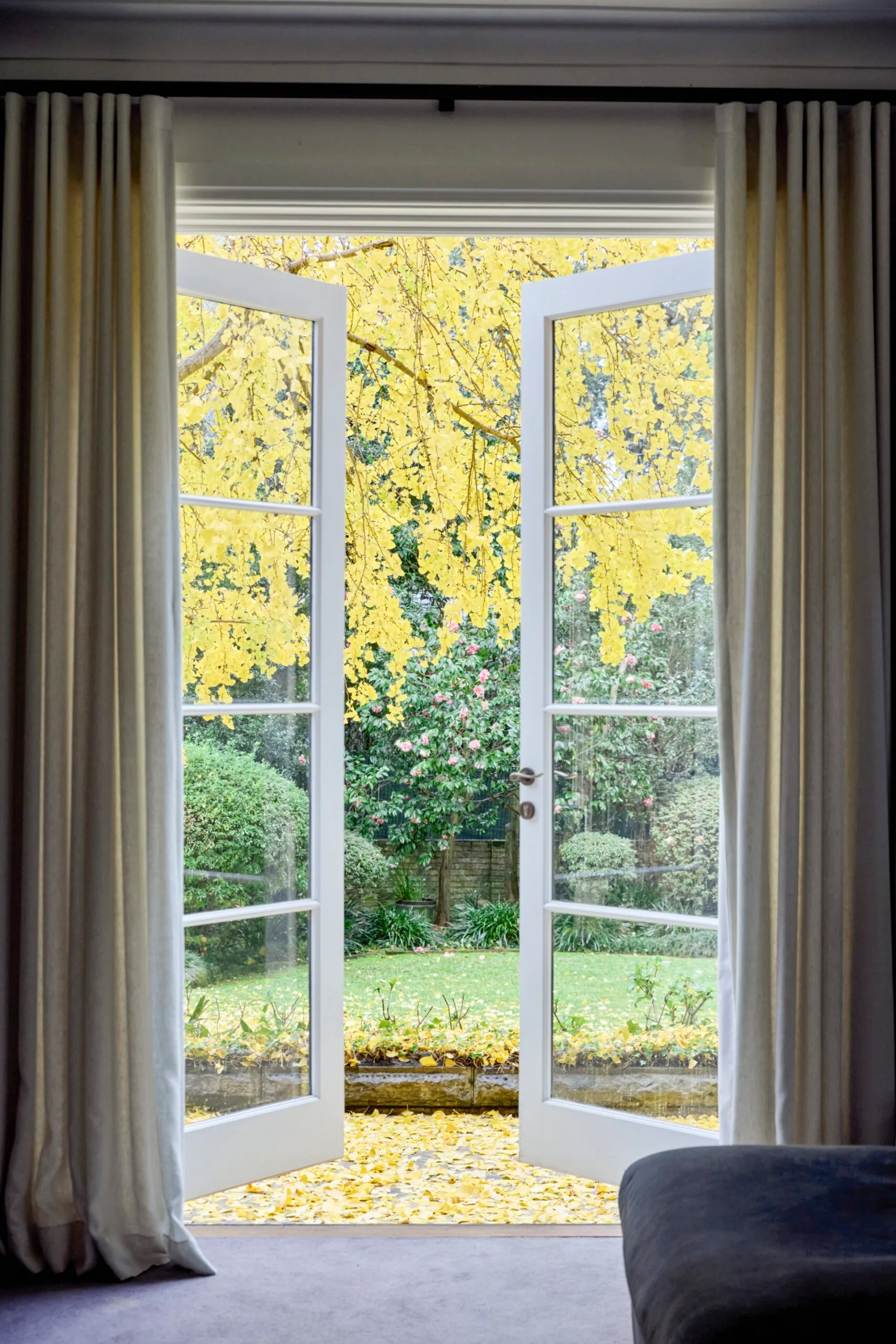 Open white French doors reveal a garden with bright yellow autumn leaves and greenery under a cloudy sky