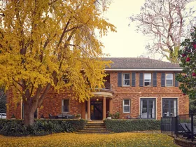 Red-brick house with a large yellow tree in front, surrounded by a garden with fallen leaves. The facade of this heritage house is a classic Georgian style.