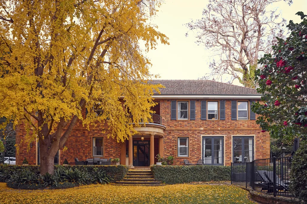 Red-brick house with a large yellow tree in front, surrounded by a garden with fallen leaves. The facade of this heritage house is a classic Georgian style.