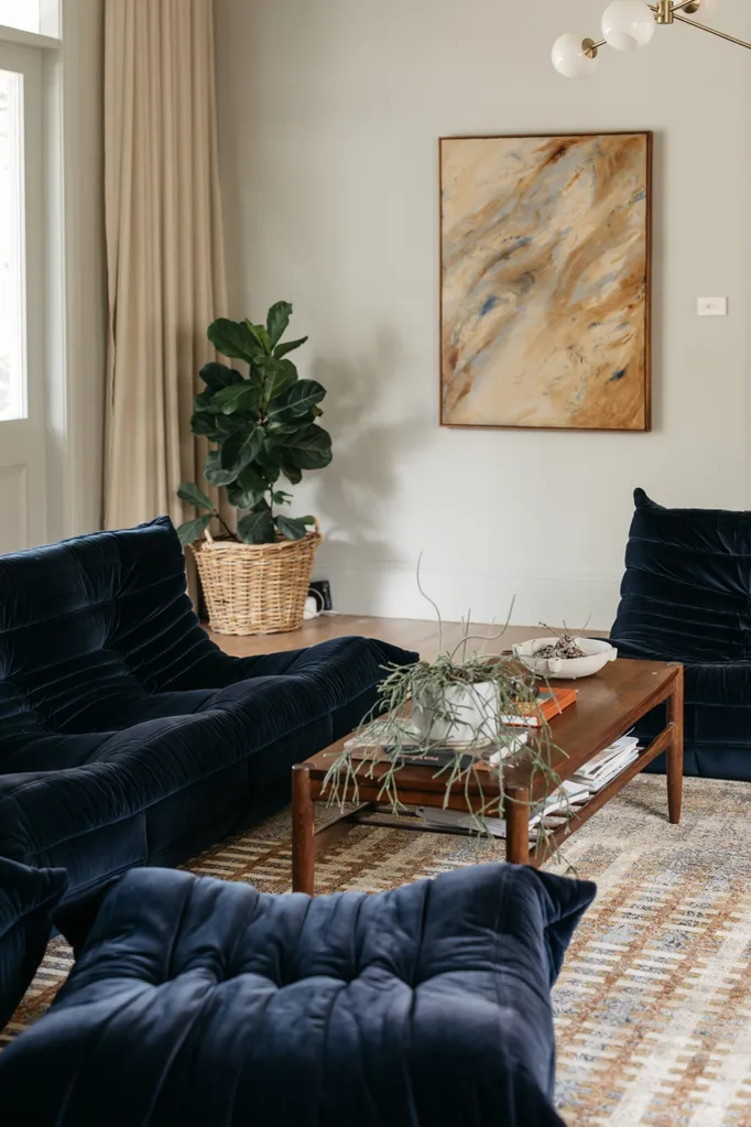 Living room in a heritage house showcasing Scandinavian style, featuring Ligne Roset Togo sofas, artwork, a midcentury coffee table and a fiddle leaf fig in a basket.