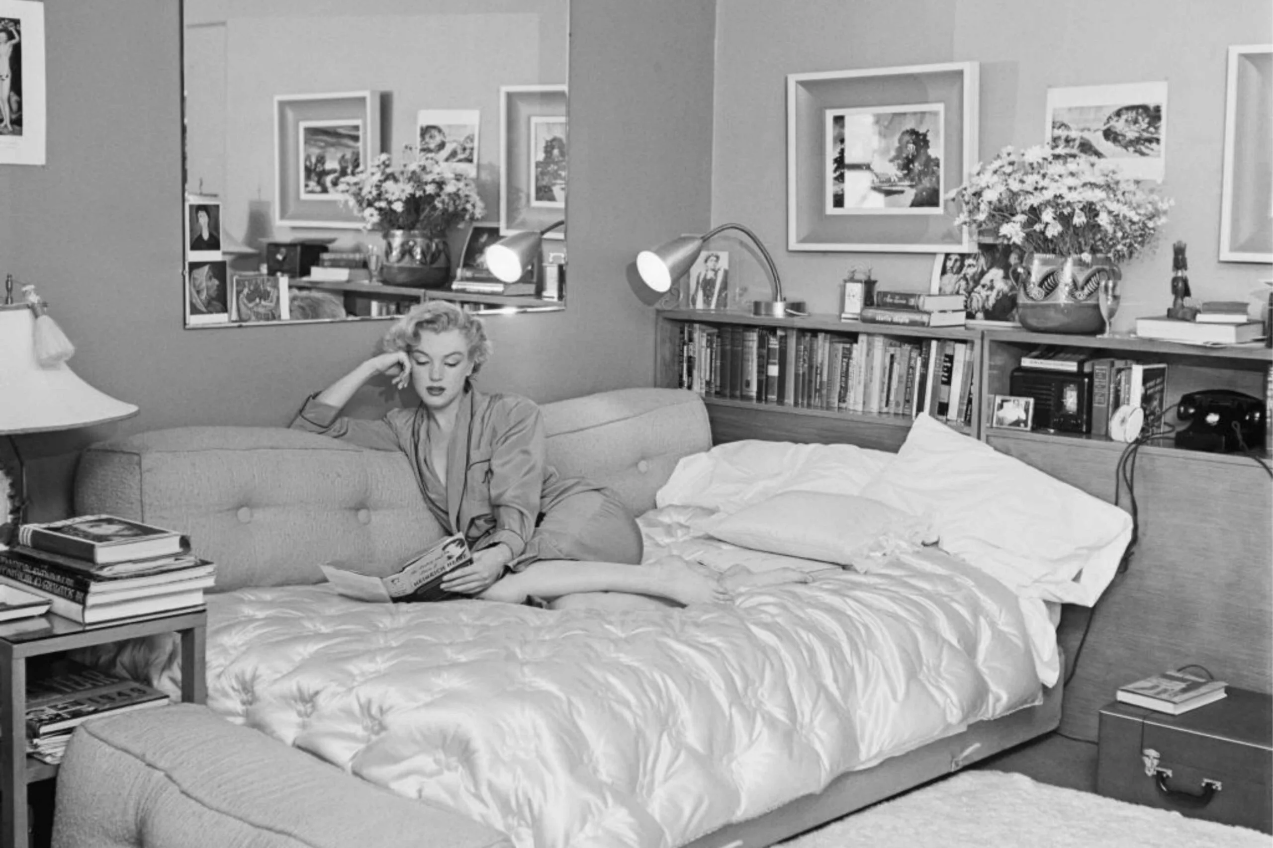 Black and white image of Marilyn Monroe on a daybed at home reading a book.