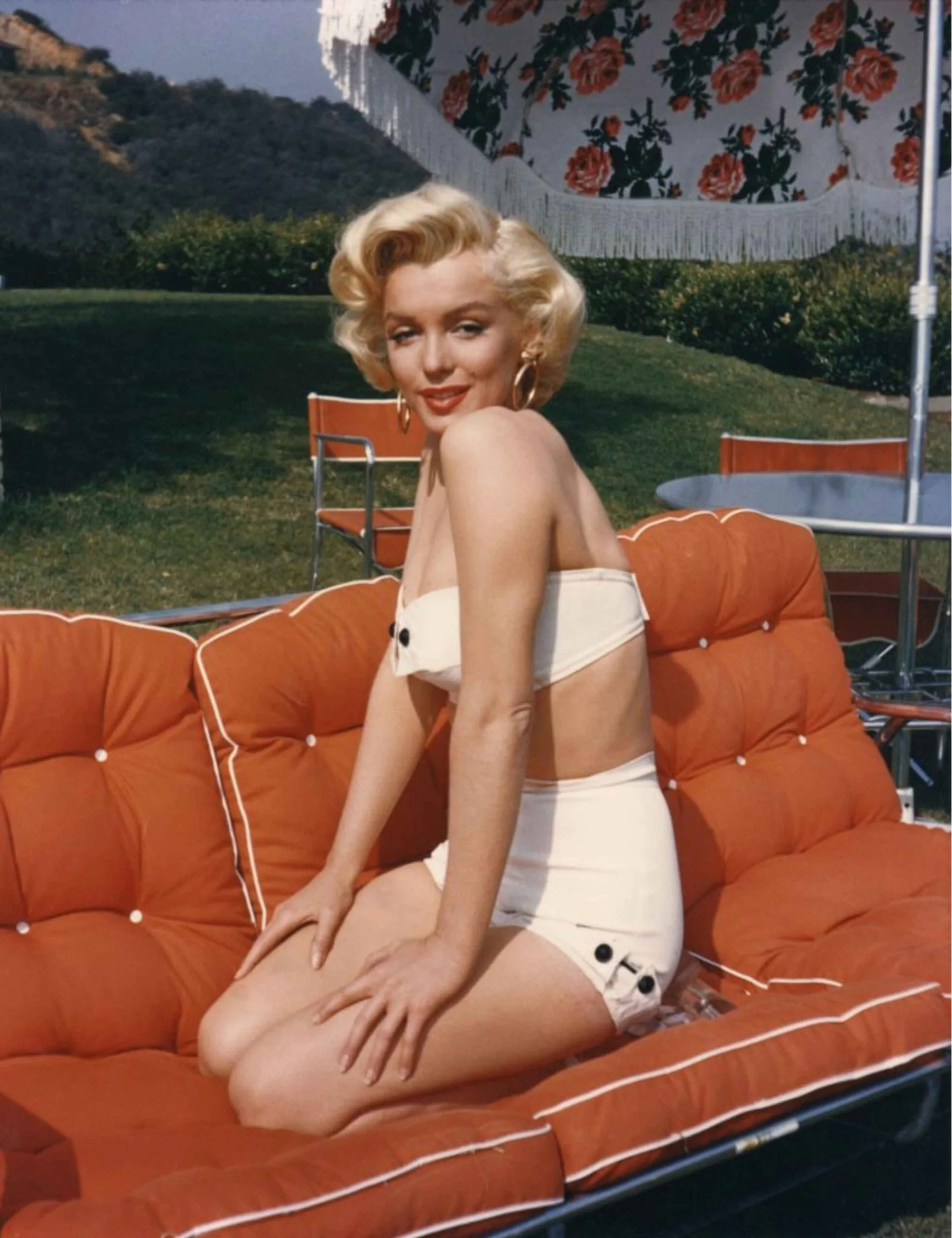 Marilyn Monroe in a bikini on an orange outdoor sofa under a sun umbrella.