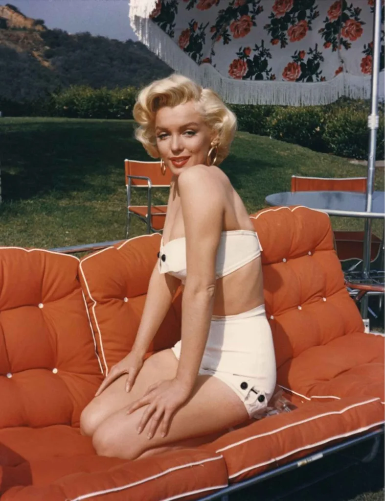 Marilyn Monroe in a bikini on an orange outdoor sofa under a sun umbrella.