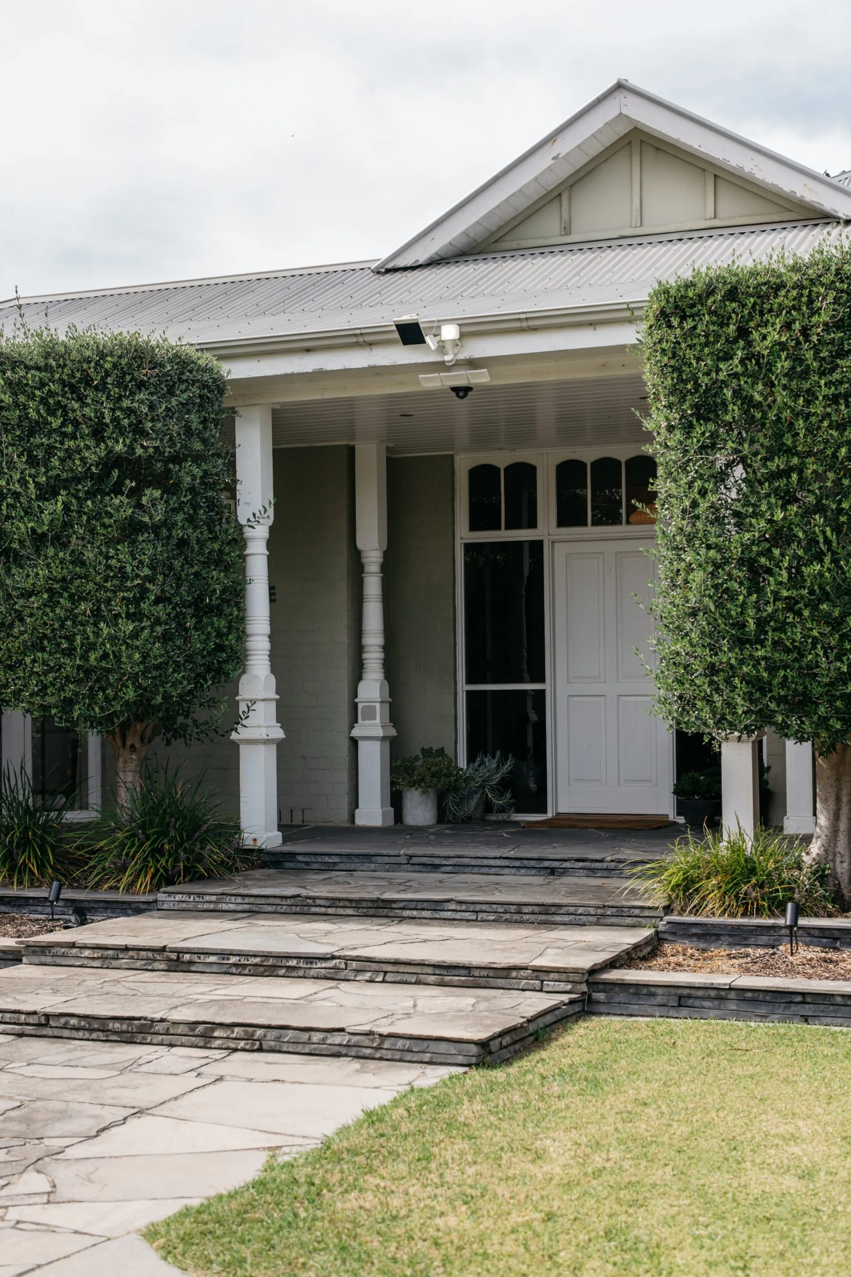 Grey and white Melbourne bayside heritage house exterior with a front porch, hedges, lawn and garden.
