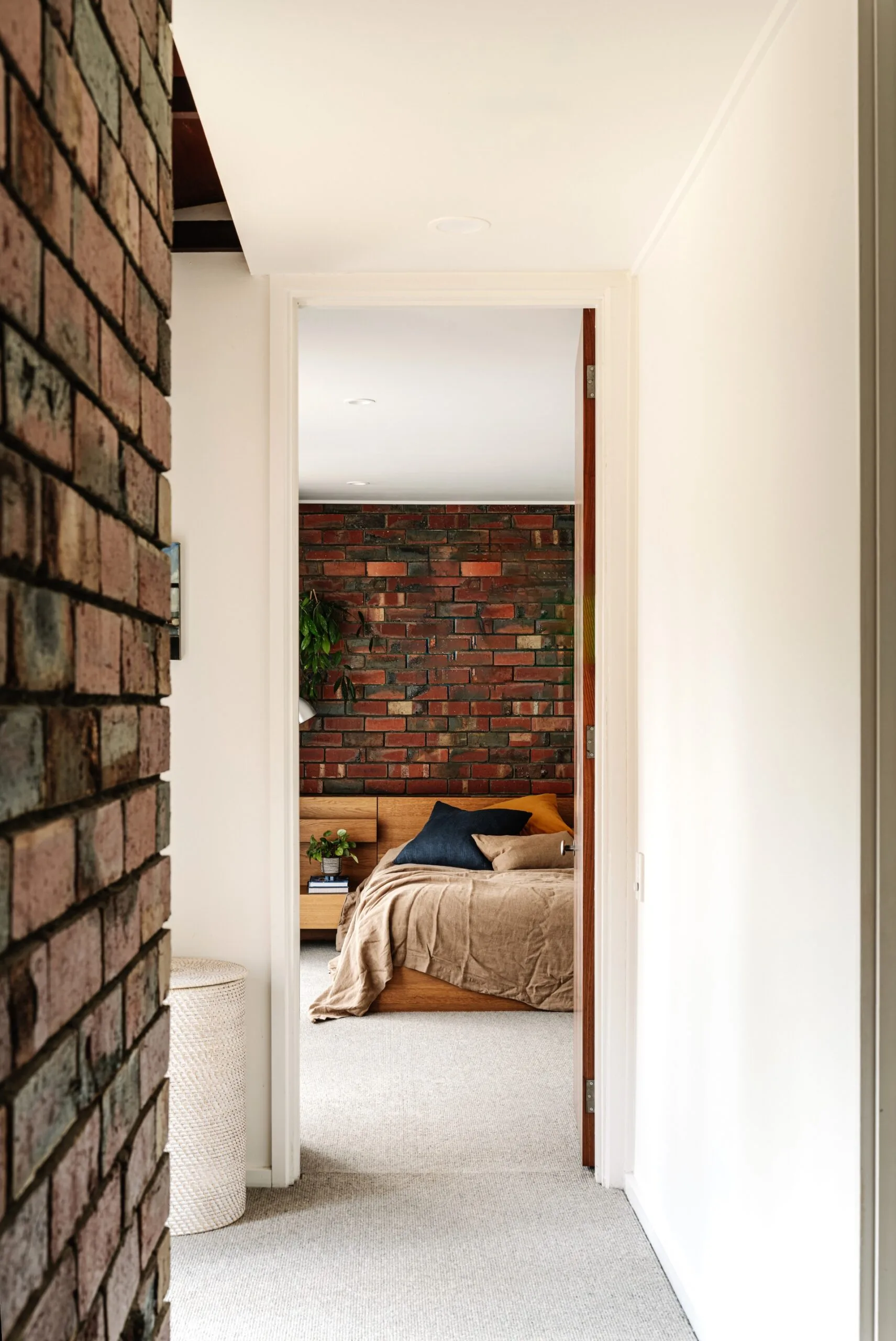 Hallway view into a cozy bedroom with a brick accent wall, wooden bed, and soft lighting. The style is mid-century.