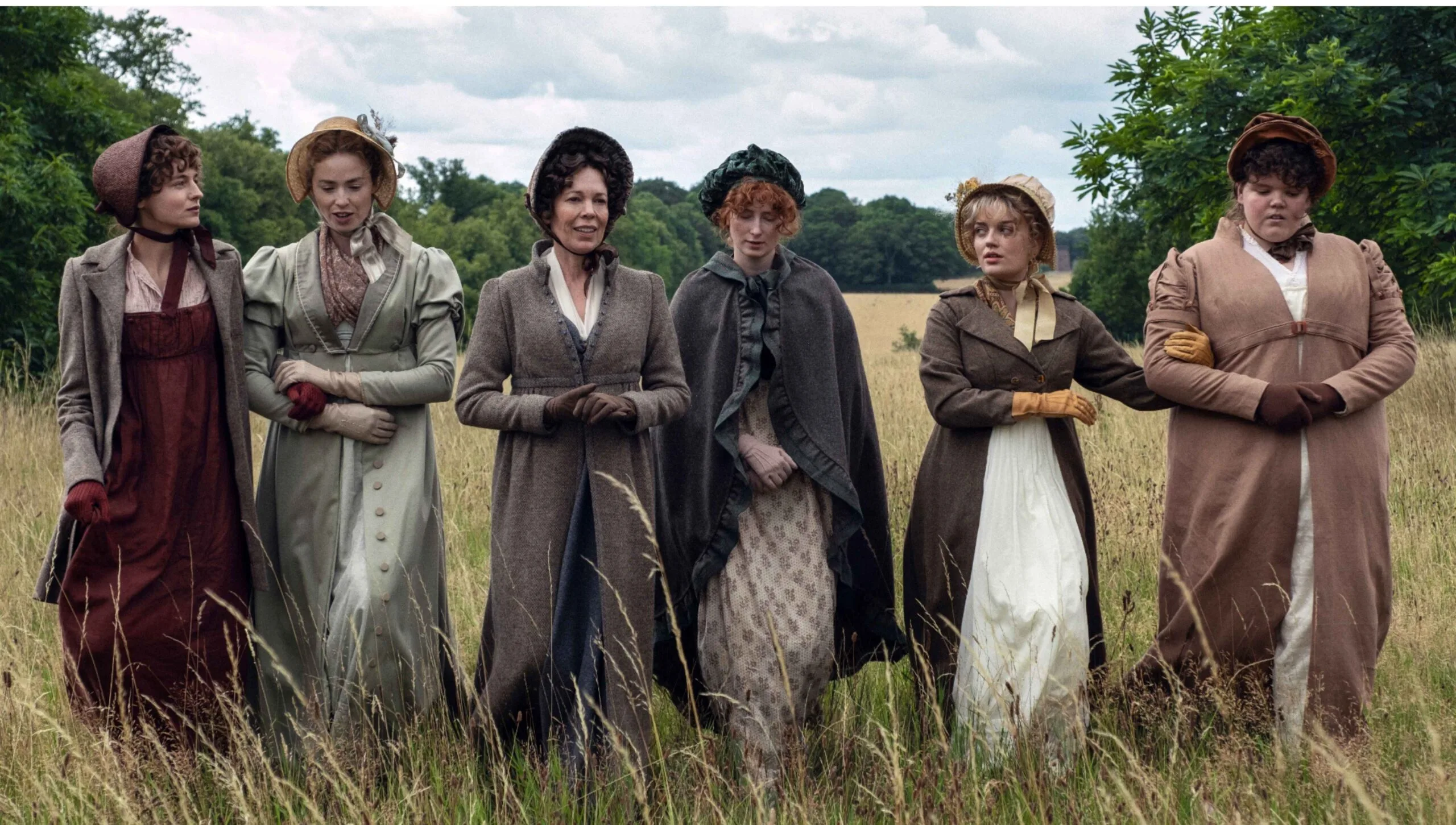 Cast of new TV series adaptation of Pride and Prejudice walking through a grassy field on location.