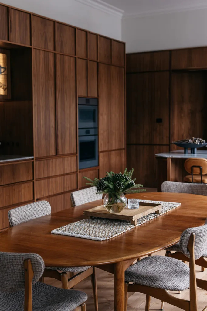 Warm kitchen featuring American walnut cabinets, wall oven and a Scandinavian-style table with upholstered chairs.