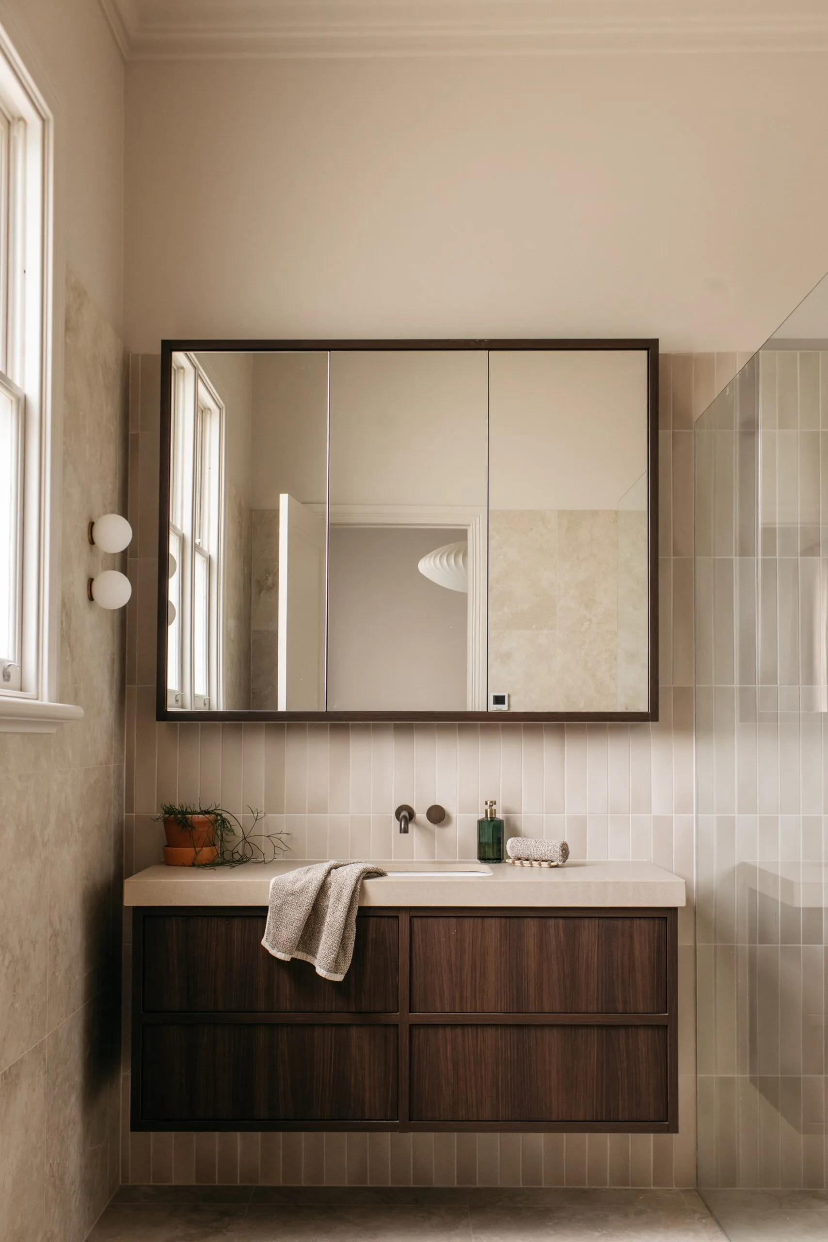 Warm neutral bathroom featuring a walnut vanity and a mirrored cabinet.