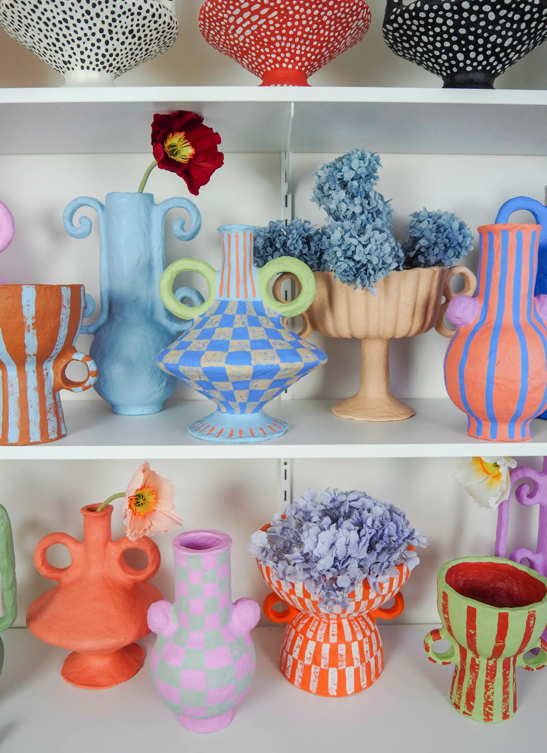 Three open shelves filled with colourful and vibrant vases.
