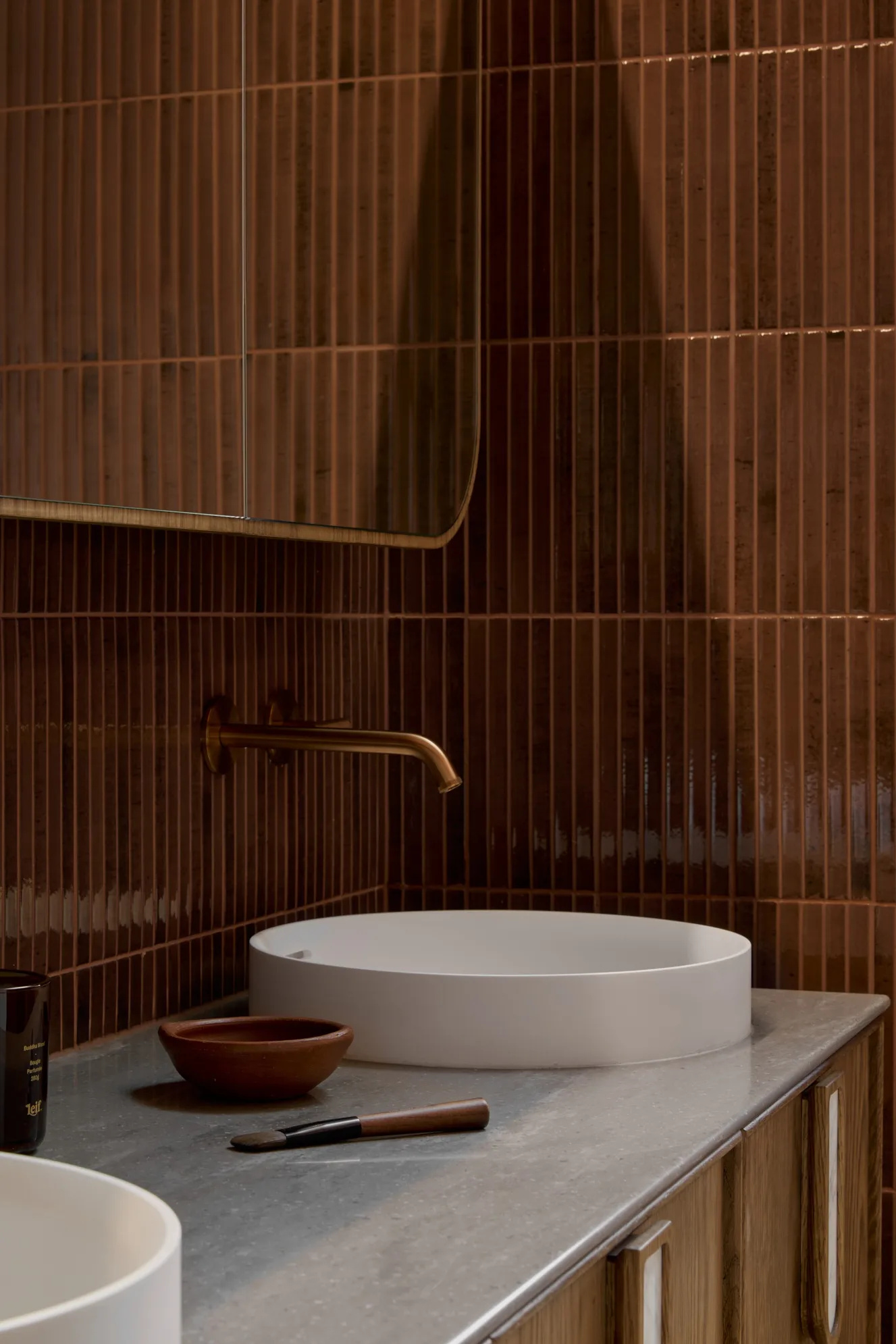 Elegant bathroom vanity with wooden vanity, two round basins on engineered stone benchtop, burgundy gloss kit-kat wall tiles, and brushed bronze faucets.