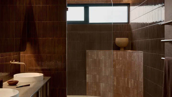 Modern bathroom with burgundy kit-kat tile walls, round basins in a marble vanity top, and a curved pink tiled half-height wall which softens a corner of the room.