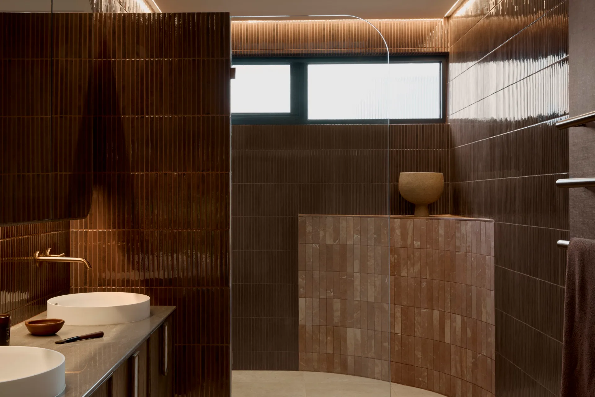 Modern bathroom with burgundy kit-kat tile walls, round basins in a marble vanity top, and a curved pink tiled half-height wall which softens a corner of the room.
