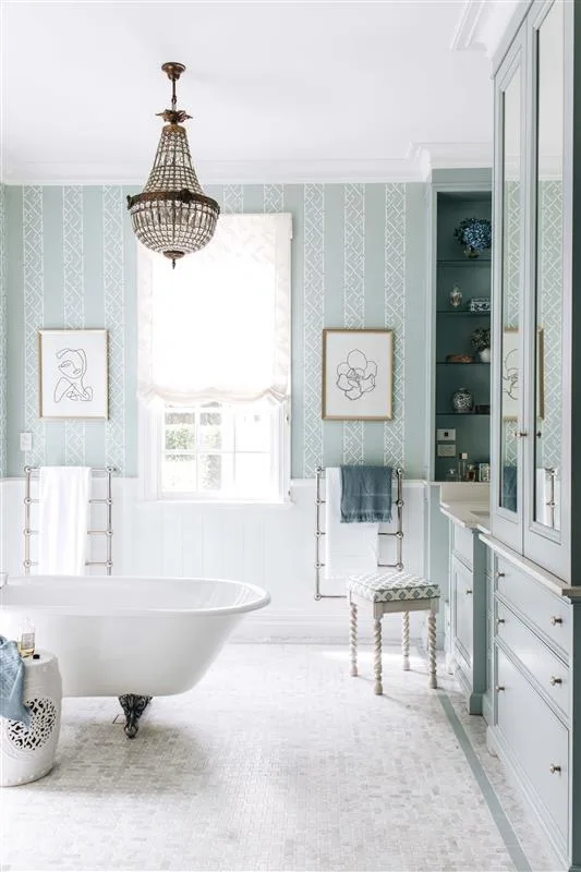 Light blue bathroom with a clawfoot bathtub, chandelier, framed art, and vanity; elegant and airy design.