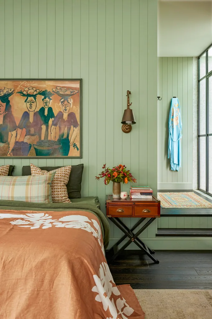 Cozy bedroom with green VJ panelled walls, a bed with floral bedding, artwork, a small bedside table with a vase of flowers on it.