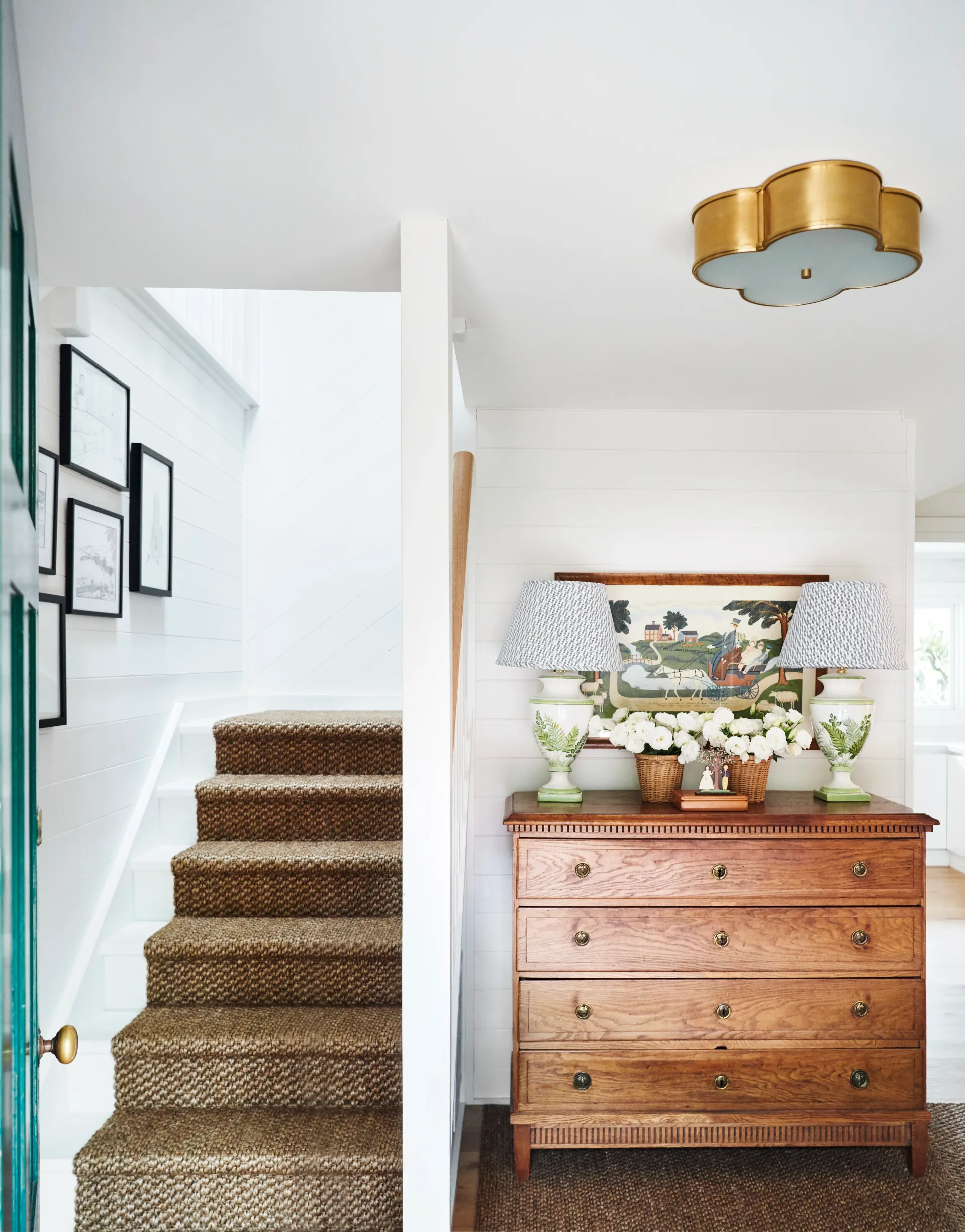 A cozy hallway with a wooden dresser, decorative lamps, and a carpeted staircase with framed pictures on the wall.