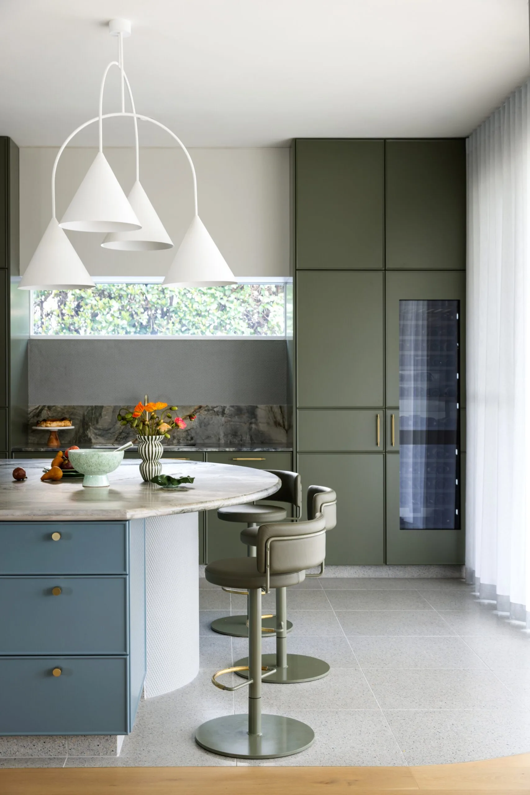 Modern kitchen with green cabinets, curved island end, white pendant lights, and green bar stools.