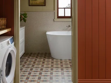 Cozy bathroom with freestanding bath tub, patterned floor tiles, and wall art, viewed through a red-paneled doorway. combined bathroom and laundry.