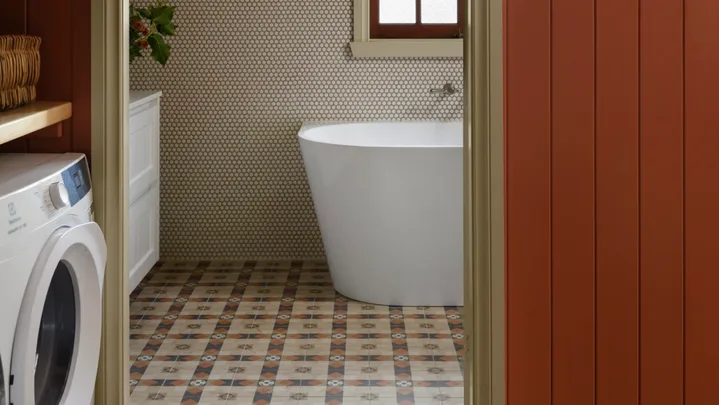 Cozy bathroom with freestanding bath tub, patterned floor tiles, and wall art, viewed through a red-paneled doorway. combined bathroom and laundry.