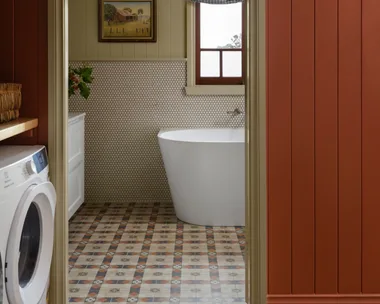 Cozy bathroom with freestanding bath tub, patterned floor tiles, and wall art, viewed through a red-paneled doorway. combined bathroom and laundry.