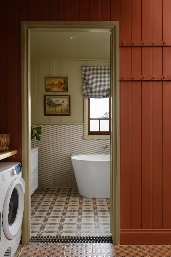 Cozy bathroom with freestanding bath tub, patterned floor tiles, and wall art, viewed through a red-paneled doorway.