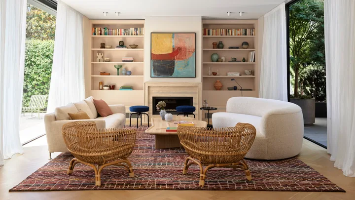 Modern living room with cream sofas, wicker chairs, abstract art, and large windows overlooking a garden.