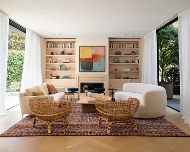 Modern living room with cream sofas, wicker chairs, abstract art, and large windows overlooking a garden.