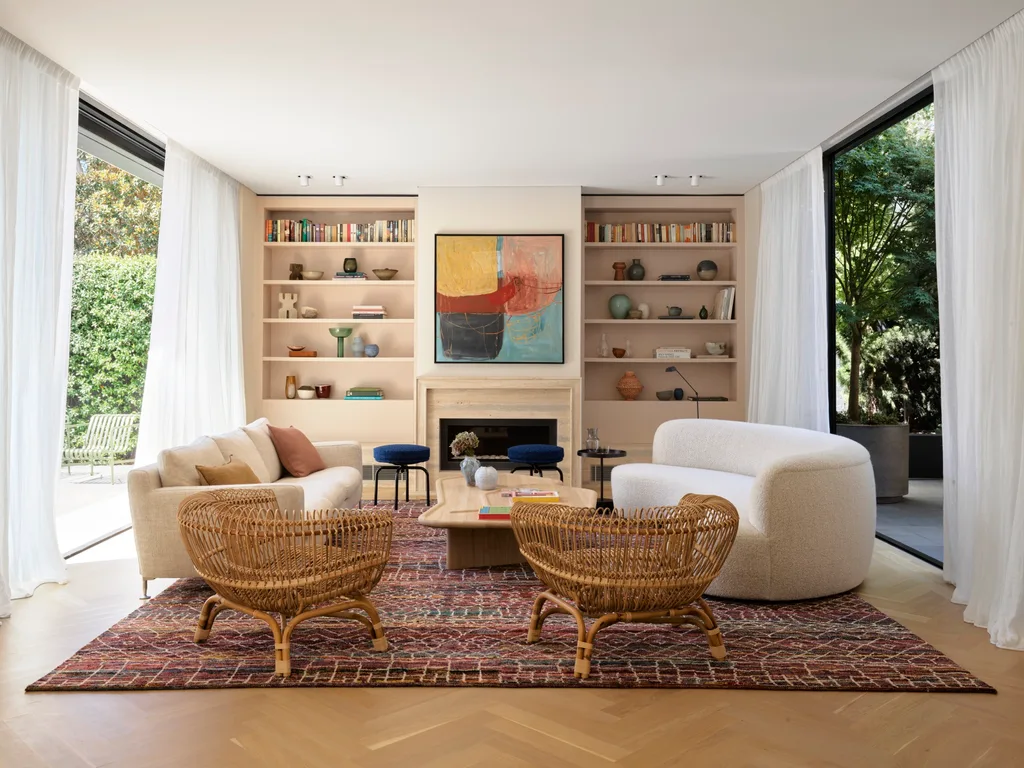 Modern living room with cream sofas, wicker chairs, abstract art, and large windows overlooking a garden.