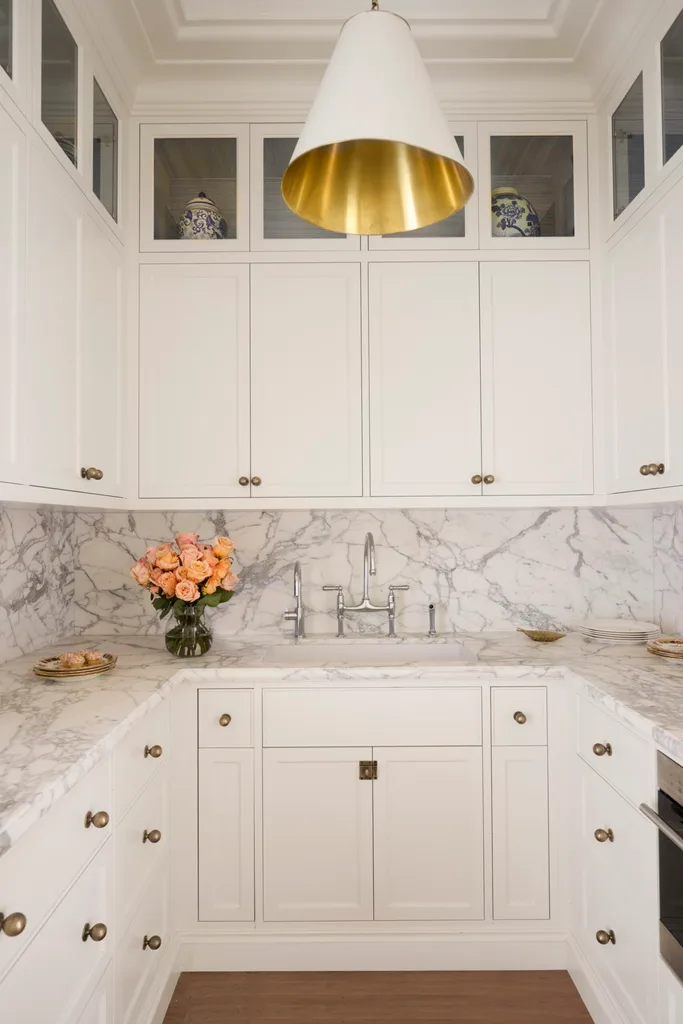 A butler's pantry with timber floorboards, white cabinets, marble countertop with a vase with pink roses on it.