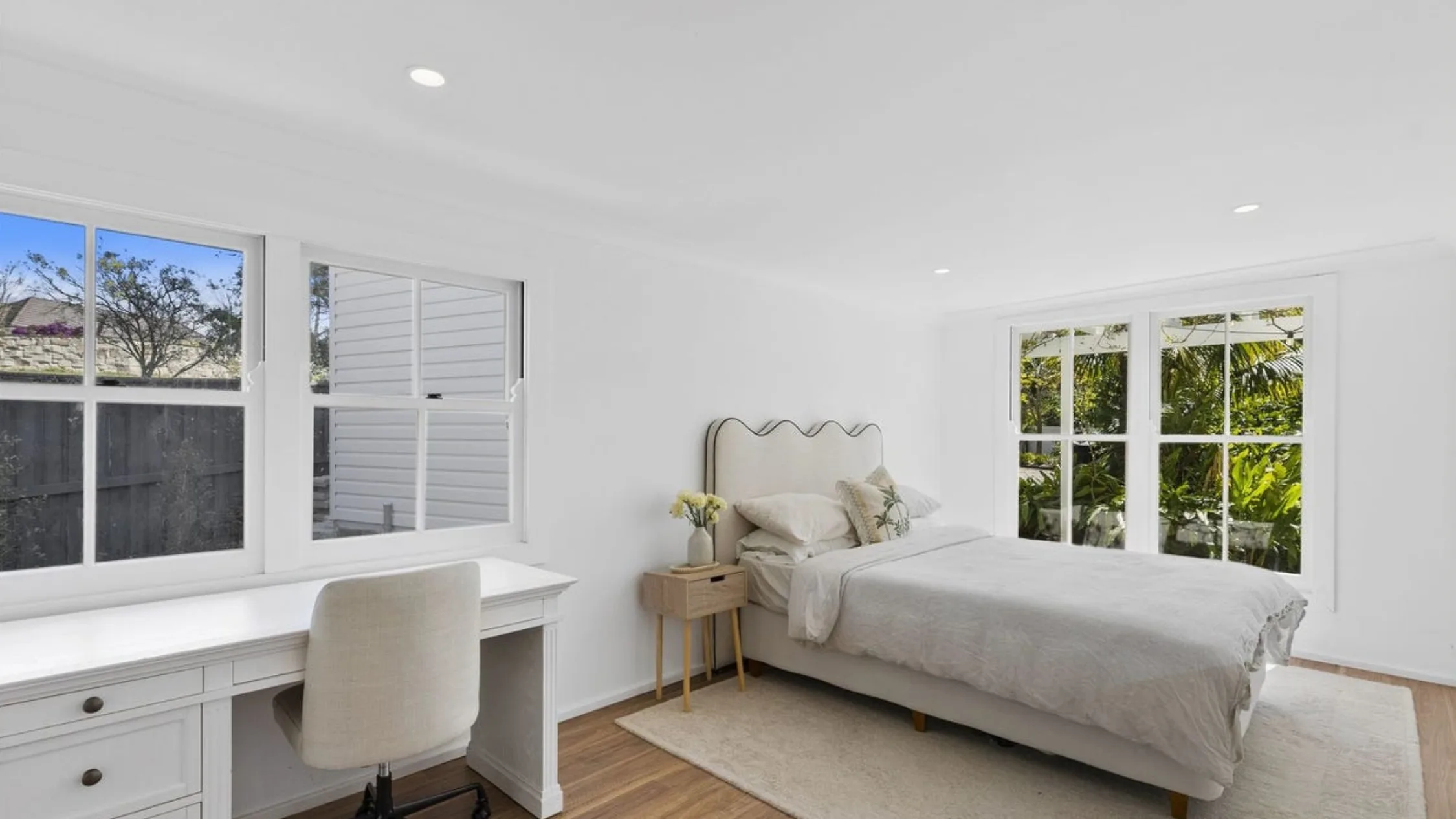 Eleanor Pendleton's Bright bedroom with a window view, white desk, chair, and bed with beige and green pillows.