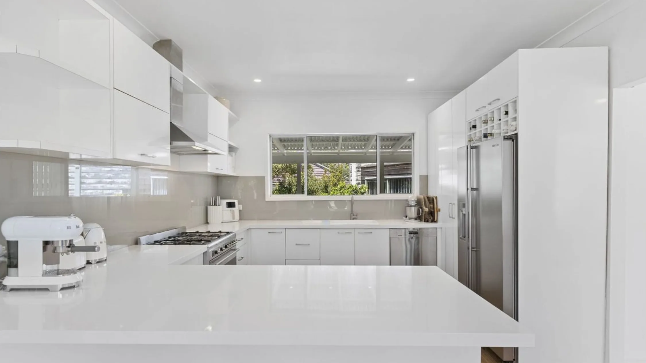 Eleanor Pendleton's Modern kitchen with white cabinets, large fridge, and a central island. Bright and spacious with a window view.