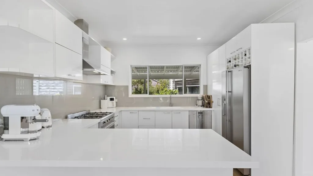 Eleanor Pendleton's Modern kitchen with white cabinets, large fridge, and a central island. Bright and spacious with a window view.