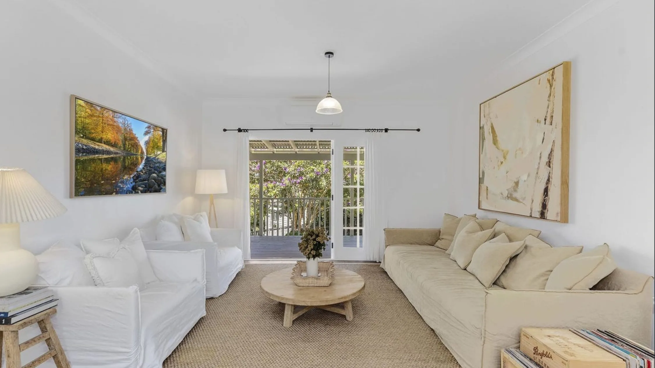 Eleanor Pendleton's Bright living room with white and beige sofas, art on walls, wooden coffee table, and glass doors leading to a patio.
