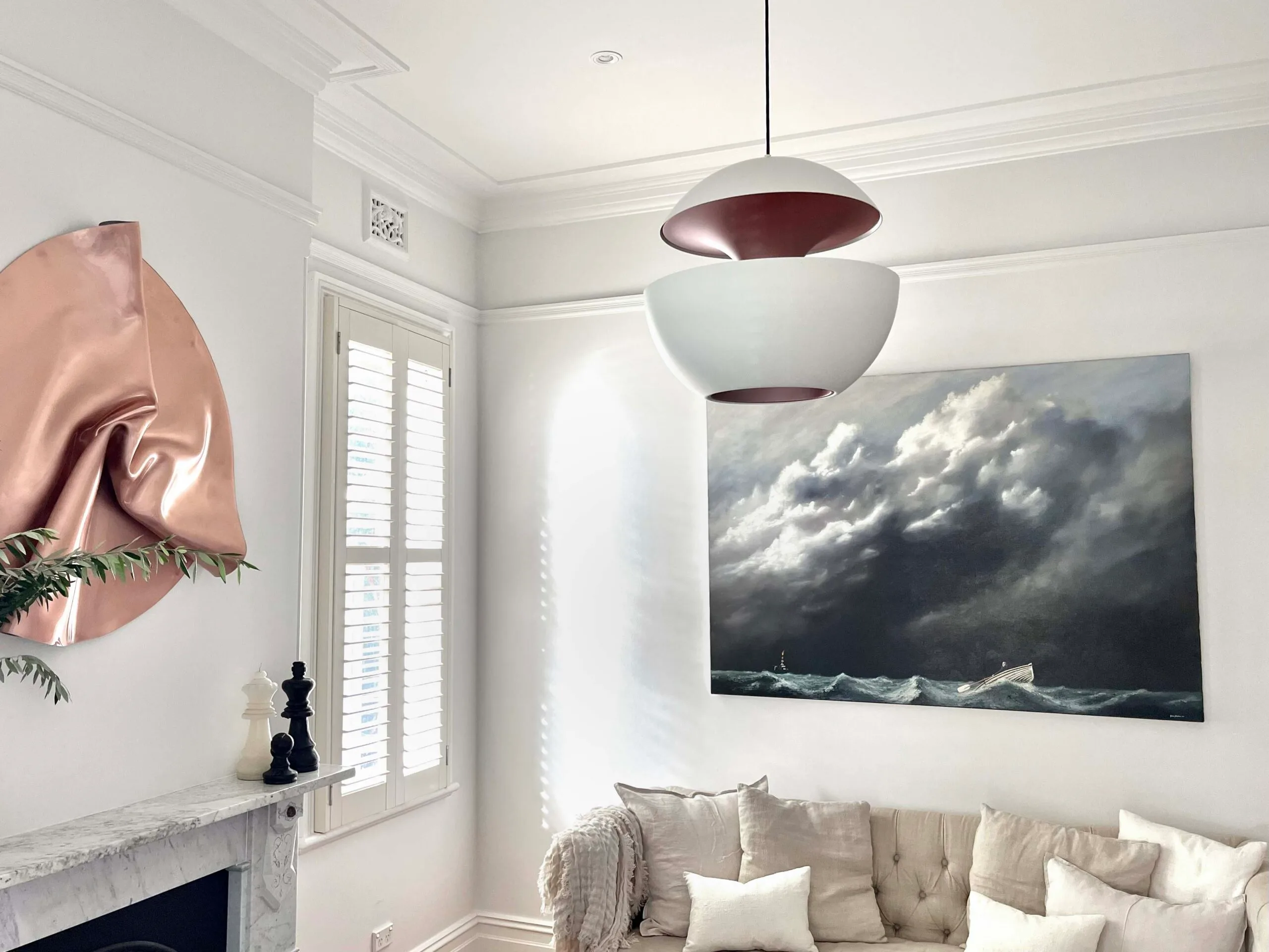 Living room with a large painting of a stormy sea, copper wall art, and a modern pendant light.