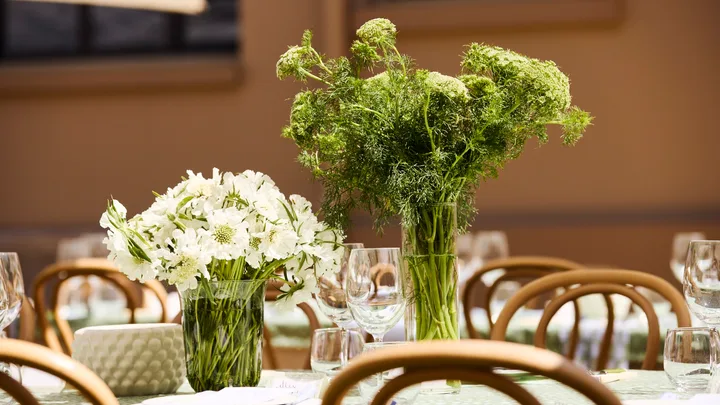Elegant table setting with vases of white and green flowers, surrounded by wooden chairs and glassware.