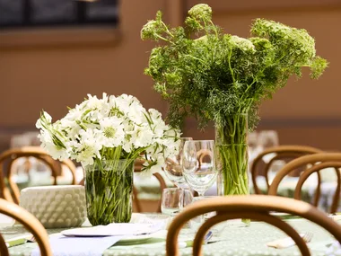 Elegant table setting with vases of white and green flowers, surrounded by wooden chairs and glassware.