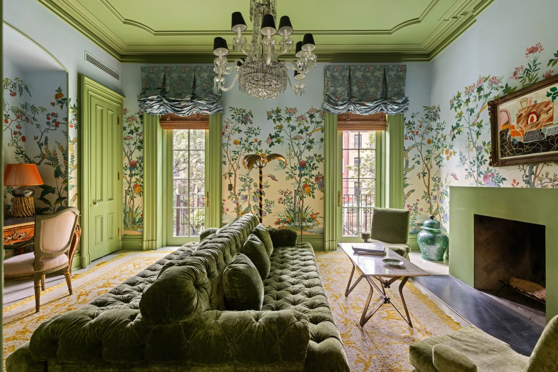 Elegant living room with green furniture, floral wallpaper, and a window overlooking a balcony. The ceiling is painted green and has a chandelier coming out of a ceiling rose. Lily Allen calls this room her "garden room"
