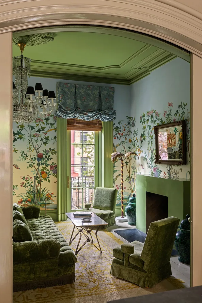Elegant living room with green furniture, floral wallpaper, chandelier, and a window overlooking a balcony. The ceiling is painted green and has a chandelier coming out of a ceiling rose.